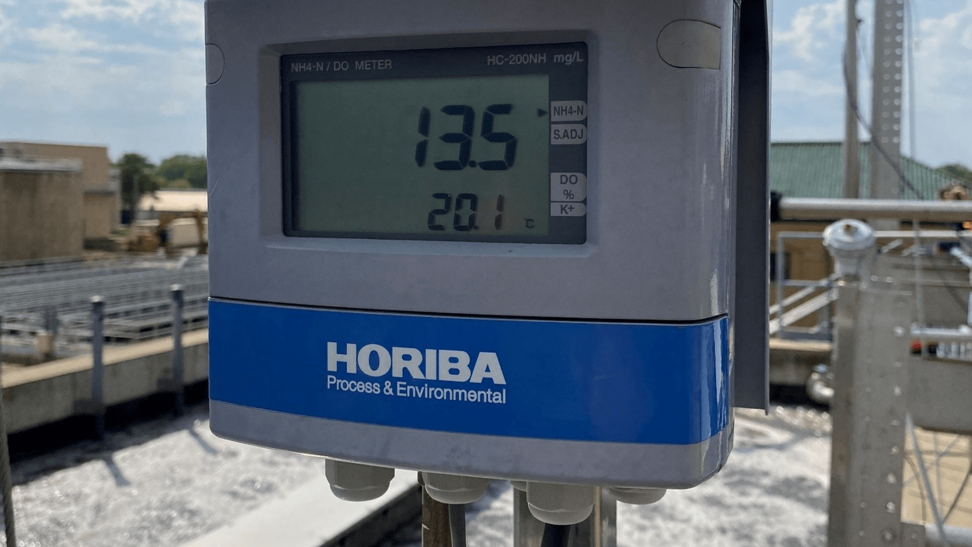 Close‑up of a HORIBA Process & Environmental sensor displaying measurements, installed beside an aeration basin at a wastewater treatment facility on a sunny day